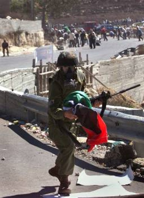 Ισραηλινός στρατιώτης με λάφυρό του από τους άοπλους διαδηλωτές τη σημαία των παλαιστινίων...