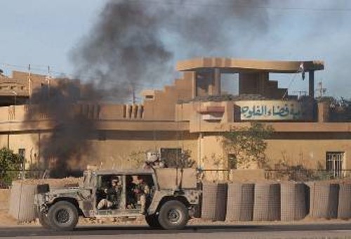 Κατοχικές δυνάμεις διέρχονται δίπλα από όχημα που φλέγεται μετά από επίθεση της ιρακινής αντίστασης